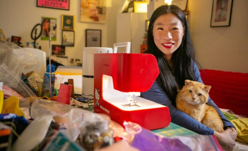 A person smiling at the camera in front of a bright red Hello Kitty sewing machine.